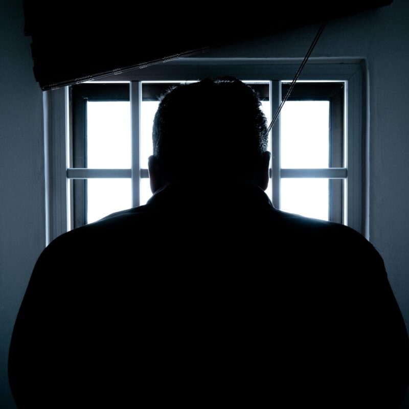 Mann steht vor einem vergitterten Fenster und blickt nach draußen
