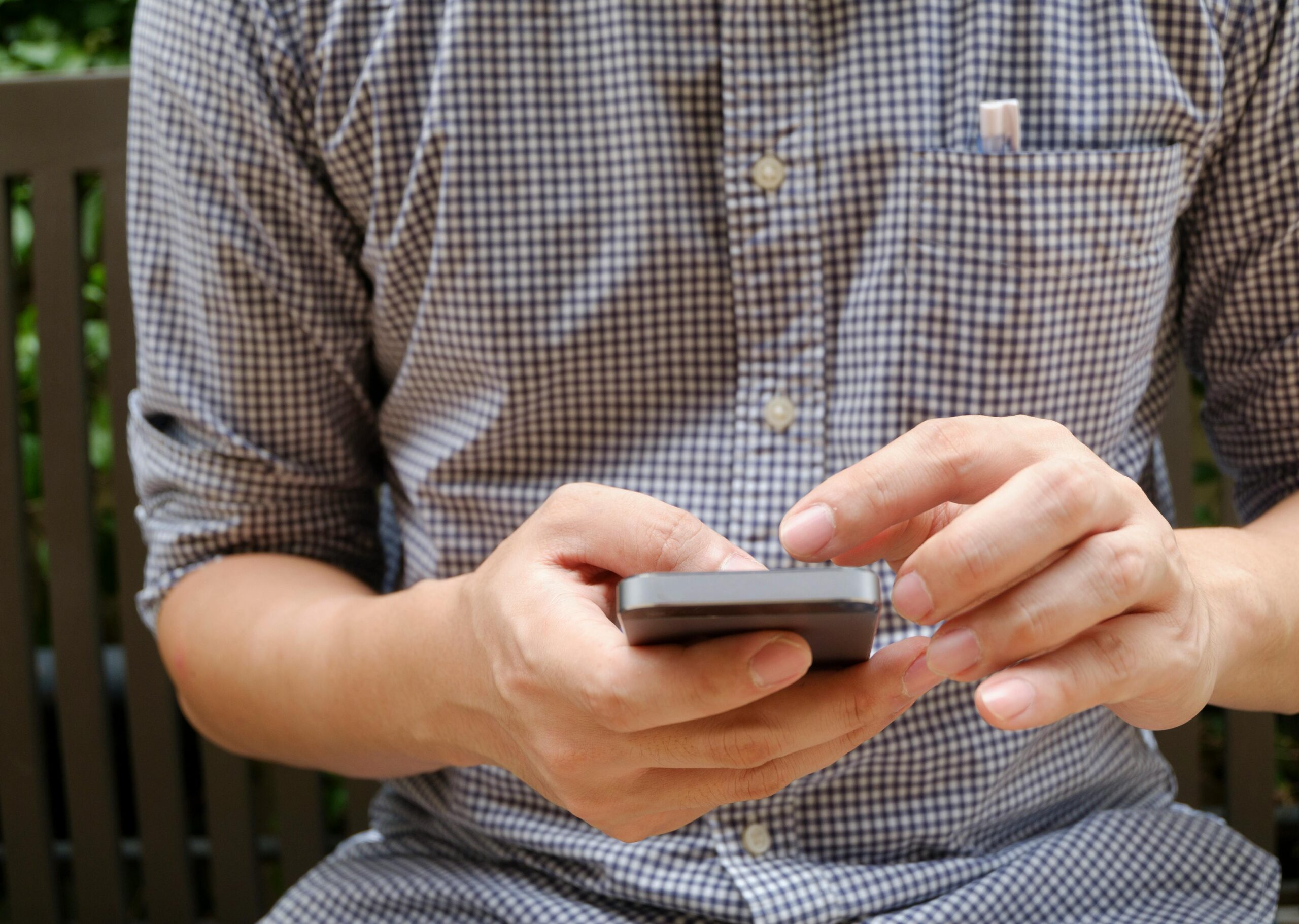 Männliche Person tippt auf Handy, welches er in der rechten Hand hält