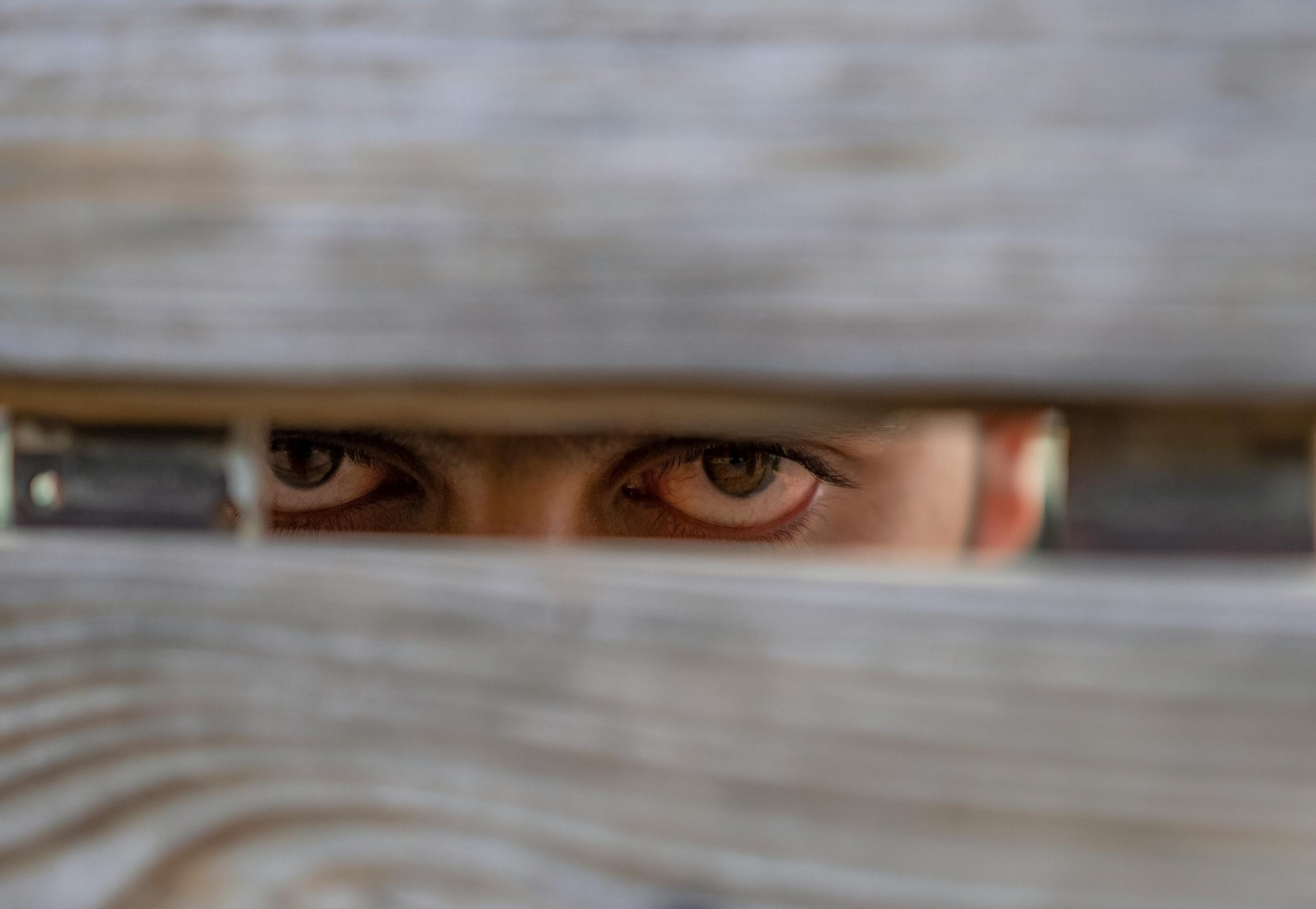 Augenpaar, das zwischen zwei Holzbalken durchsieht